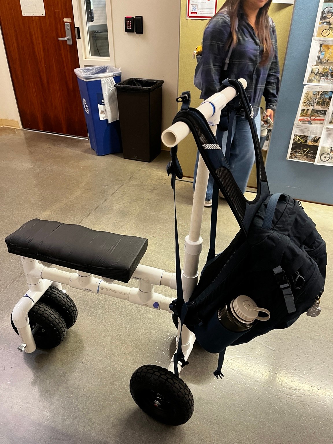 Side view of the PVC knee scooter carrying a backpack from the handlebars